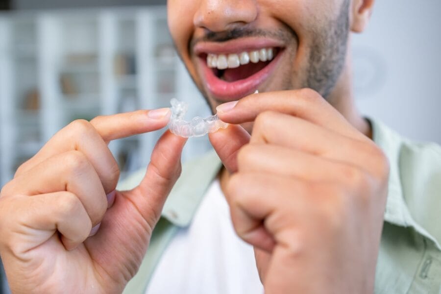 Close-up Of A Man's Hand Putting Transparent Aligner In Teeth