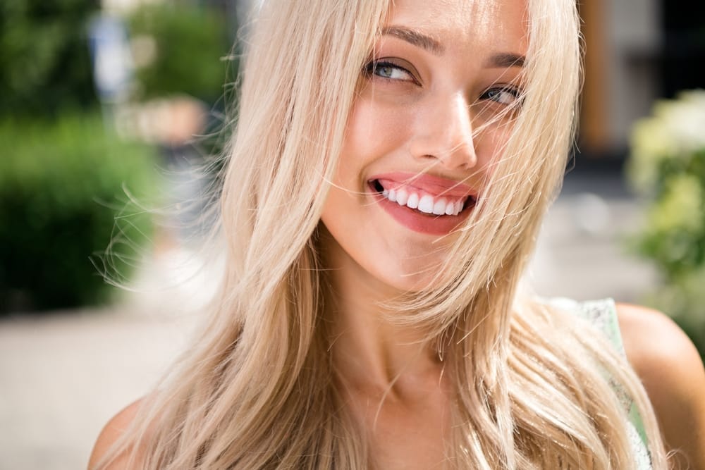 A woman with long hair smiles brightly while taking a selfie indoors - Dentist Atlanta