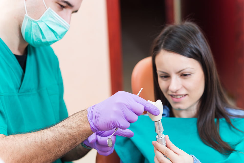 Dentist showing to his patient a dental implant with crown - Dental Crowns in Atlanta, GA