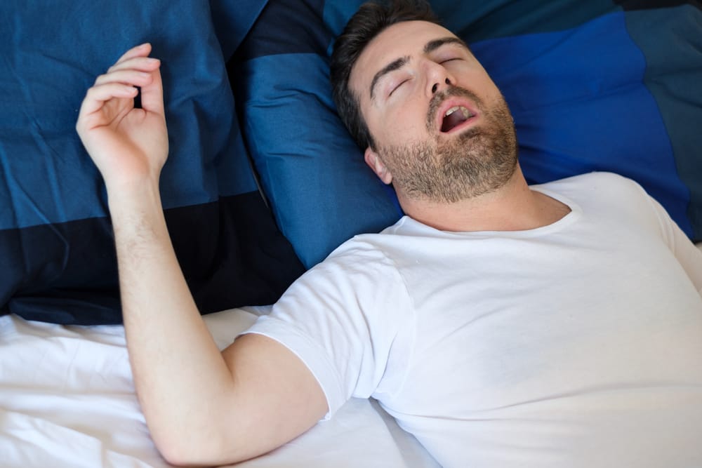 A woman looks frustrated in bed, covering her ears with a pillow while a man beside her snores loudly - Dentist Atlanta