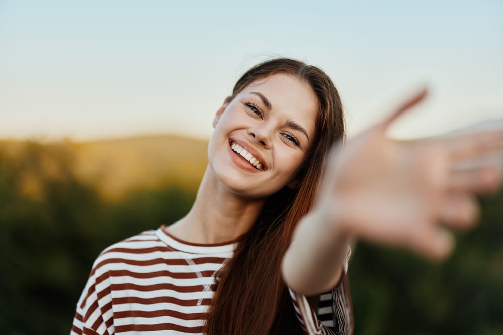 A woman with long hair smiles brightly while taking a selfie indoors - Dentist Atlanta