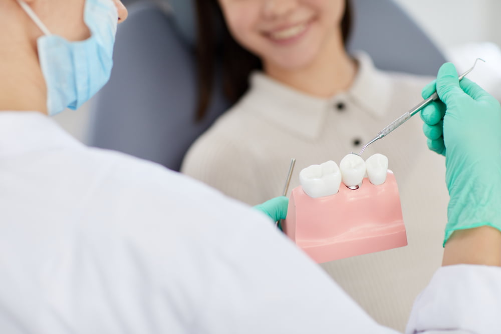 A dentist explains a dental procedure using a model of teeth while the patient smiles in the background - Dentist Atlanta A dentist explains a dental procedure using a model of teeth while the patient smiles in the background - Dentist Atlanta